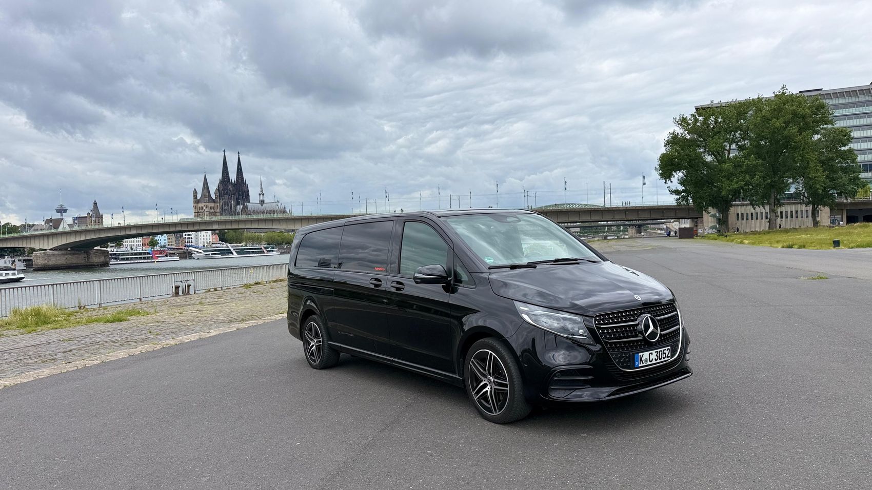 Schwarze Mercedes-Benz V-Klasse am Rheinufer mit Blick auf den Kölner Dom